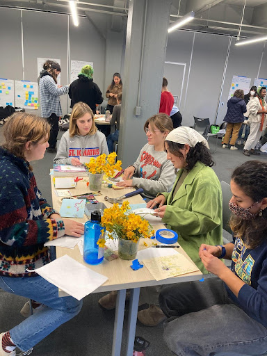 Five people sitting around a rectangle table filled with paper, tape, and pens