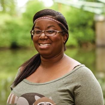 Charissa Jones smiles, wearing glasses, a brown patterned headband, and green shirt while standing outdoors.  