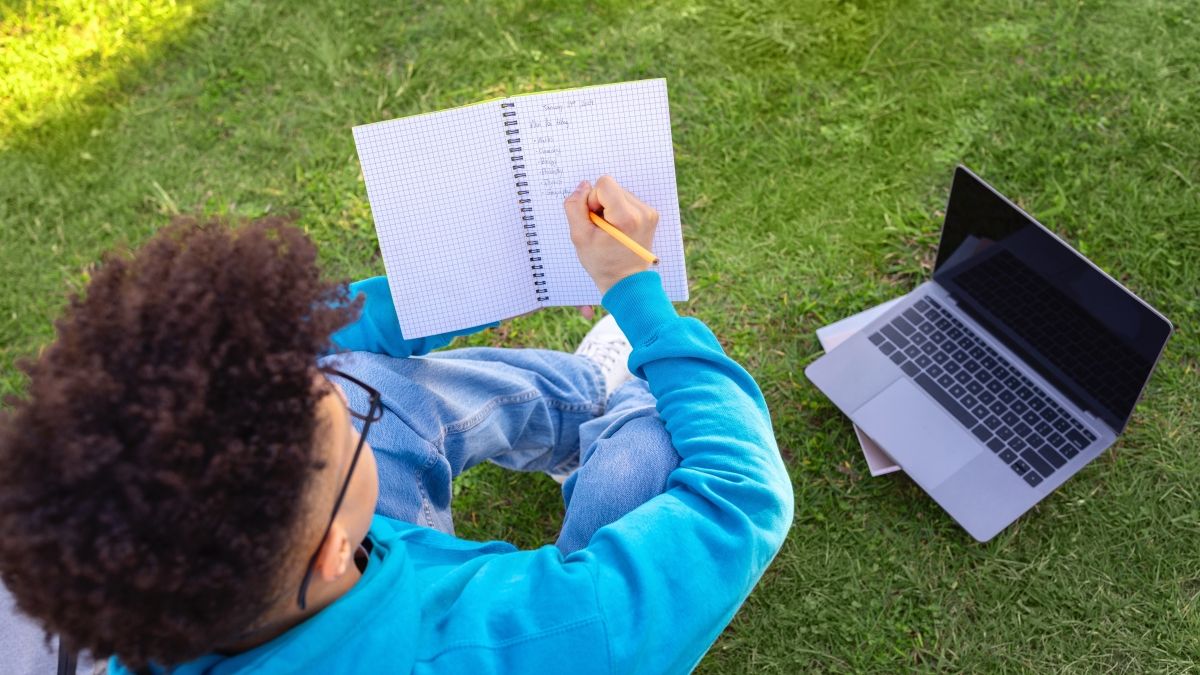 Student writing in notebook with laptop nearby