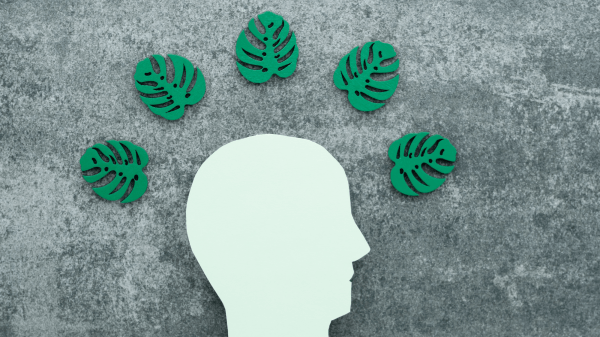 A cutout silhouette of a head in white is below five green leaf cutouts, all against a gray textured background