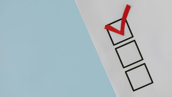 Part of a piece of paper is seen above a light blue background; the paper has three checkboxes, the top one filled in with a red check mark