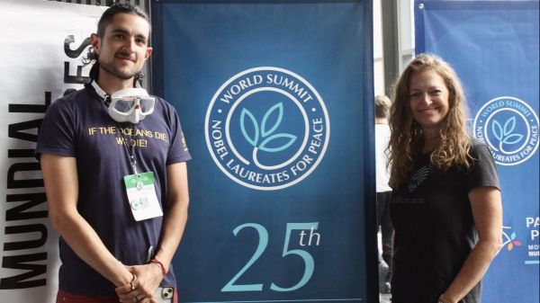 Billion Acts of Peace Fellowship Mentor at Monterrey, Mexico 2024; two people stand on either side of a "25th Founding Anniversary, World Summit Nobel Laureates for Peace" banner