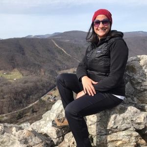 A smiling woman sitting on the edge of a high ridge