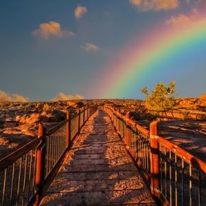 Photo of stone bridge in a rocky landscape with a rainbow arching from the center of the photo to the right