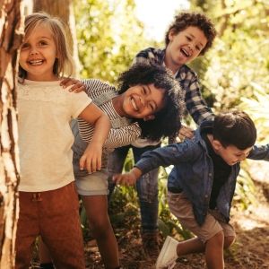 Young children peek behind a tree during autumn